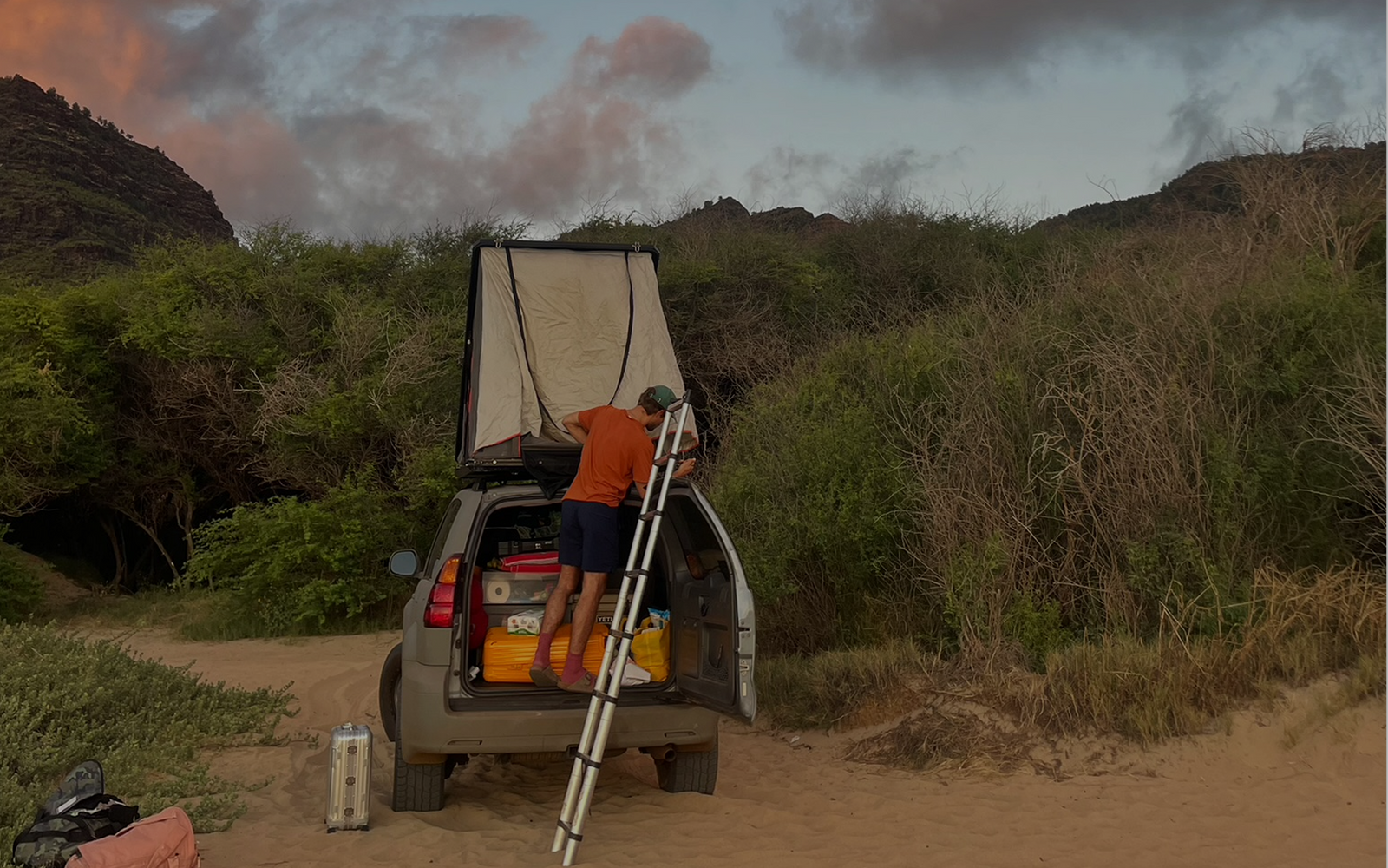 Person setting up a tent on the back of a car in beachy sand dunes